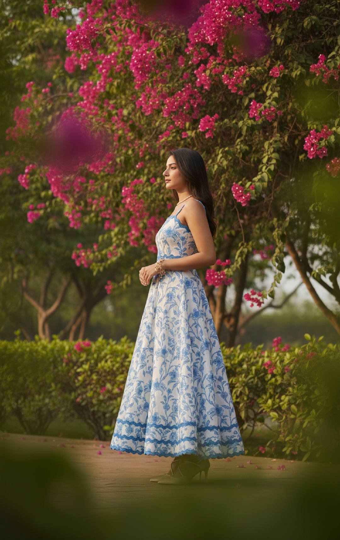 Woman in a blue floral dress standing in a garden with pink flowers