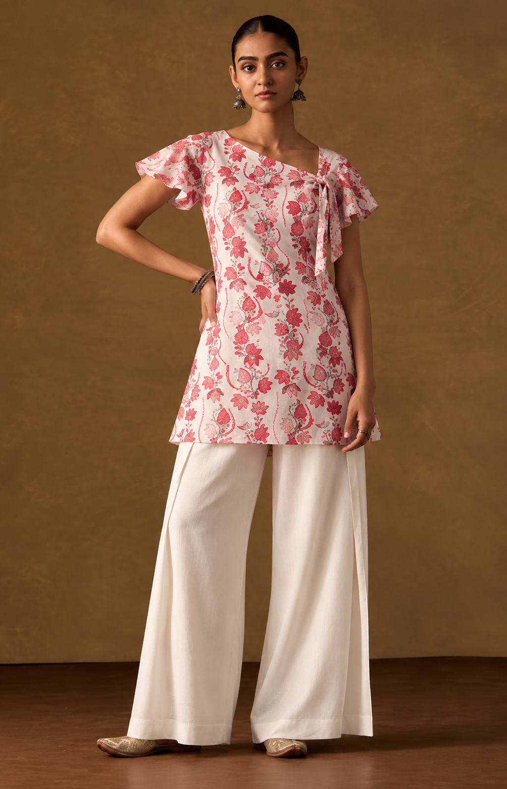 Model wearing a blush short kurti with rose floral print, flutter sleeves, and neckline tie