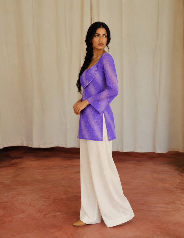 Model wearing a violet short kurti with curved stitch detailing, long sleeves, and side slits